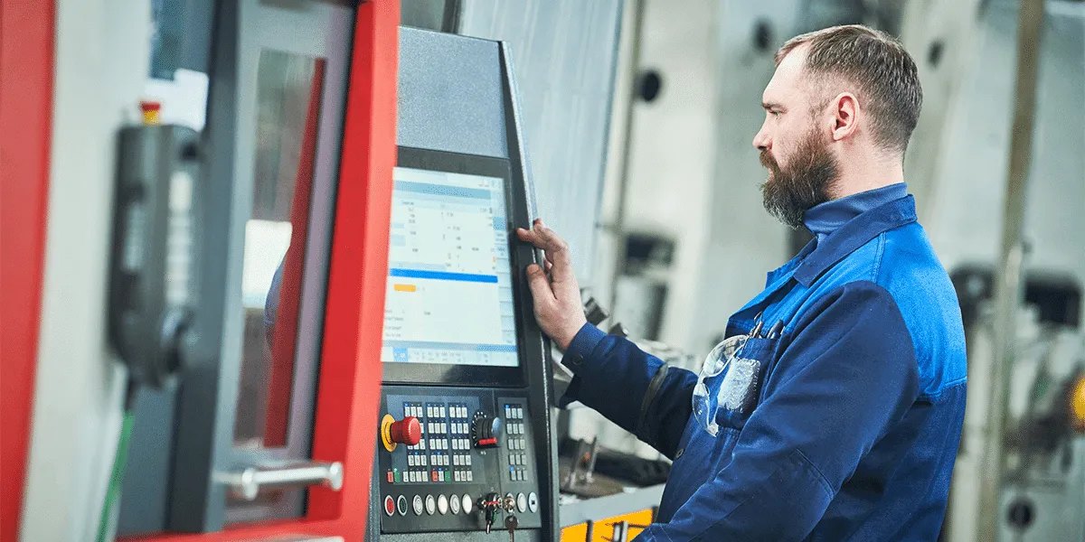 A machinist reading job data on the screen at a CNC machine's control station.